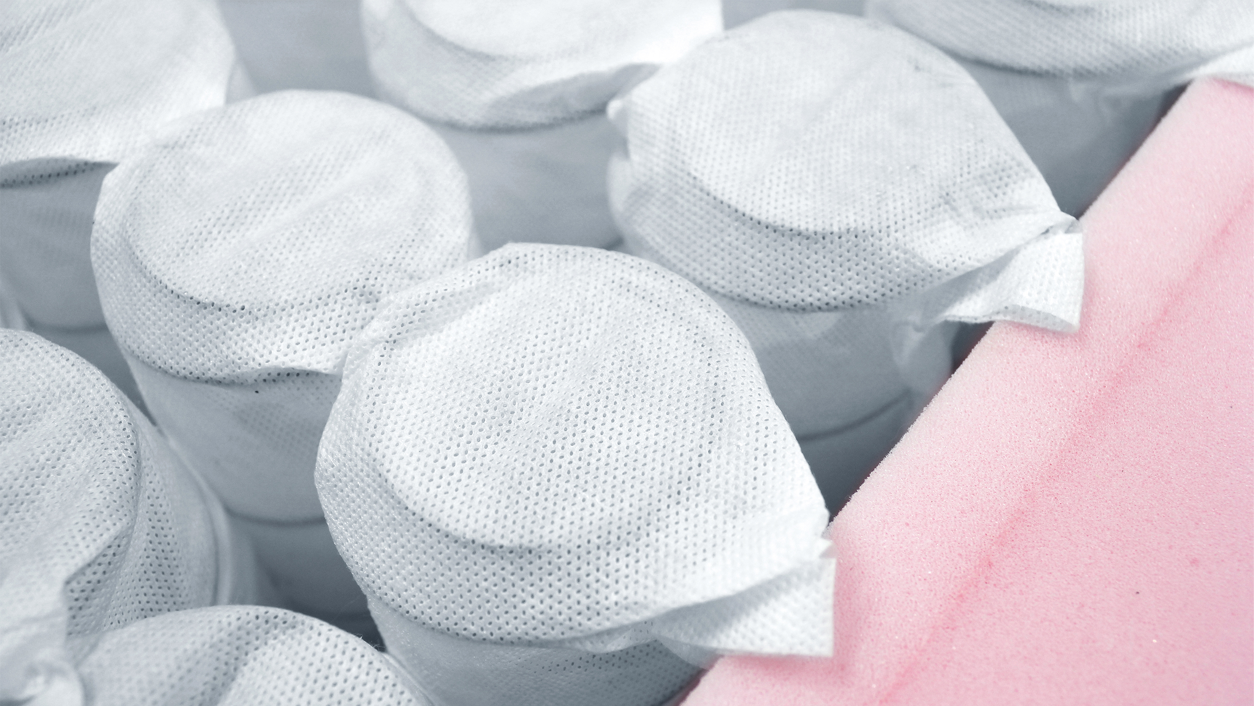 Nahaufnahme von umhüllten Boxsprings in einer Matratze, neben einer rosa Schaumstoffschicht.