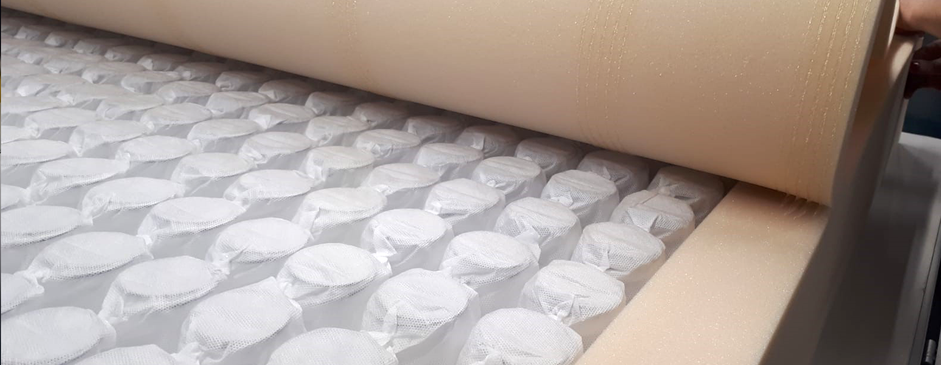 Schaumstoffrolle wird über eine Reihe von verpackten Federn in einer Matratzenproduktion gerollt.