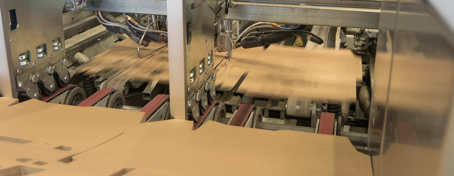 Maschine formt und transportiert Kartonverpackungen auf einem Förderband.